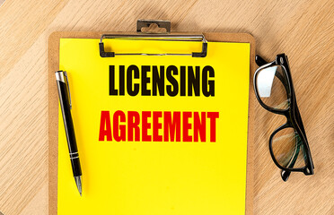 Clipboard with the text licensing agreement on a wooden desk with a pen and glasses