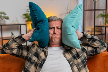 Repair work at neighbors. Irritated Caucasian man cover ears with pillows annoyed by noisy loud...