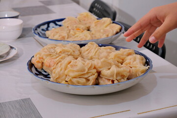 A hand reaches for a plate with the traditional Central Asian dish manty