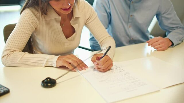 Camera view of couple signing agreement. People sitting at table and placing their initials on important documents. Woman and man completing contract in office. Collaboration. Partnership concept.