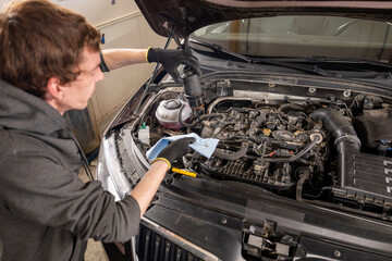 Mechanic in gloves servicing a car engine with tools and cloth in a well-lit garage, concept of...