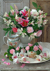 Lilies, camellias, alstroemeria and orchid flowers in a vase on a table against a rustic background still life