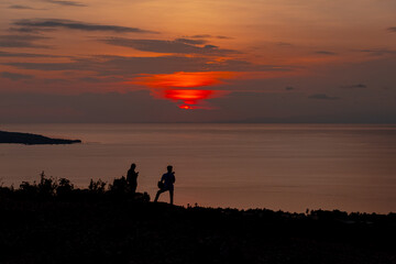 Fototapeta premium Silhouetted Figures Witnessing a Breathtaking Sunset by the Ocean