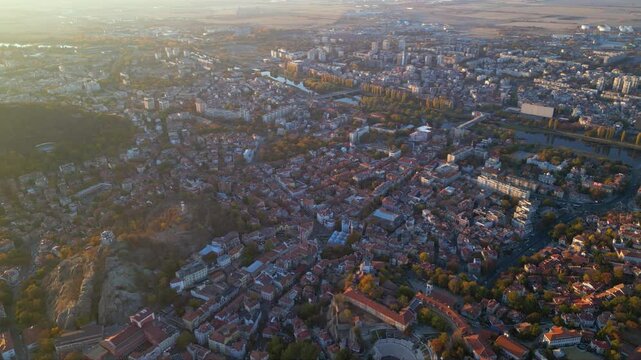 Aerial drone footage of a sunset over the city of Plovdiv in Bulgaria. Ancient city of Filipopolis filmed from above on a warm autumn afternoon. European city seen from a helicopter establishing shot.