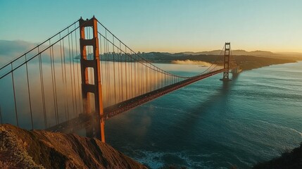 Fototapeta premium The Golden Gate Bridge shrouded in mist during sunrise, with golden hues breaking through the fog