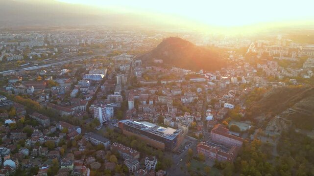 Aerial drone footage of a sunset over the city of Plovdiv in Bulgaria. Ancient city of Filipopolis filmed from above on a warm autumn afternoon. European city seen from a helicopter establishing shot.