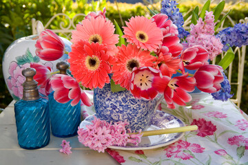 Still life of red tulips, pink gerbera, and pink and blue hyacinths in vases on a table outdoors