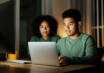 Focused young professionals collaborating at night on laptop in modern office