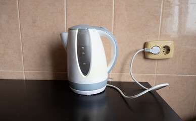 An electric kettle with water stands on the table in the kitchen, plugged into the socket