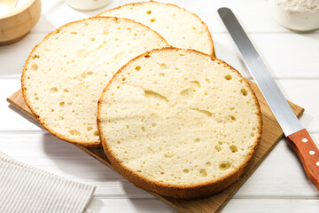Delicious cut sponge cake and knife on white wooden table