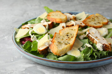 Tasty Caesar salad with chicken on gray textured table, closeup