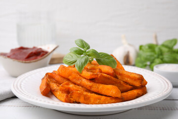 Sweet potato fries and basil on light wooden table, closeup
