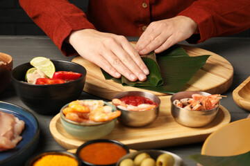 Woman wrapping food into banana leaf at wooden table with products, closeup. Healthy eco serving