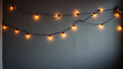 A string of warm white fairy lights strung across a textured gray wall, casting a warm glow in the otherwise dark room.