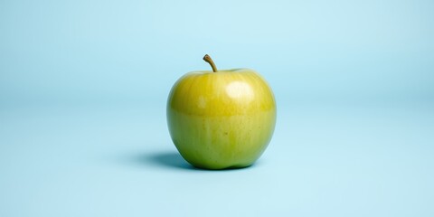 A single green apple sits on a light blue background, showcasing its vibrant color and smooth texture.