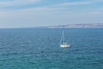 Obraz premium Serene ocean view with white sailboat on deep blue waters near coastal landscape