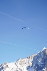 Paraglider soaring above snowy peak on clear day
