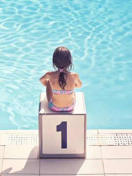 Una bambina di spalle &egrave; seduta sul blocco di partenza di una piscina, il blocco &egrave; il numero uno. Concetta della difficile competizione delle donne per emergere nella societ&agrave;.