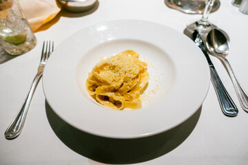 A creamy plate of fettuccine Alfredo rests on a white tablecloth, the rich sauce glistening under soft light, accompanied by polished silverware and a neatly folded napkin.