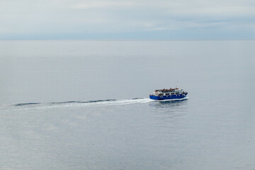 Blue ferry sails peacefully across calm open sea with scattered passengers onboard enjoying a serene journey.