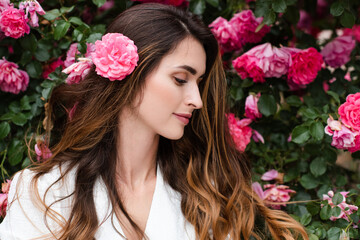 Naklejka premium Beautiful young woman 25-29 year old with long blonde hair posing with pink rose flowers in garden outdoors. Springtime.