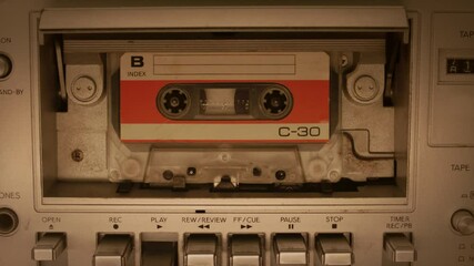 Cassette tape playing in a deck. Close-up of a plastic, audio cassette tape playing in a vintage tape deck, evoking nostalgia for retro music technology - Powered by Adobe