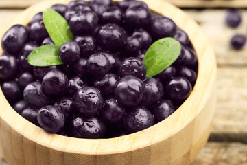 Ripe acai berries and leaves in bowl on table, closeup