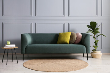 Comfortable sofa, houseplant and side table near grey wall in room