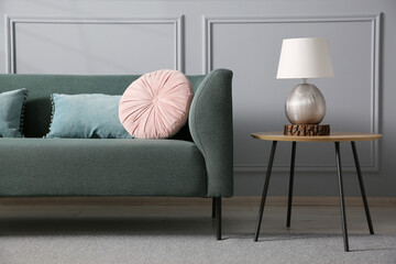 Comfortable sofa and side table near grey wall in room