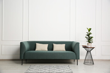 Stylish sofa, pillows and side table with houseplant near white wall indoors