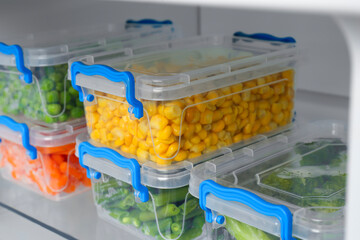 Plastic containers with different frozen vegetables in refrigerator, closeup