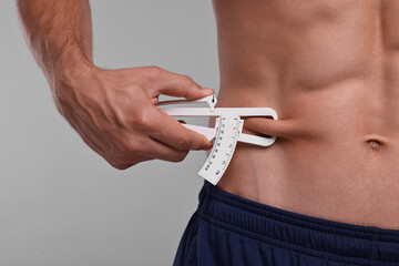 Man measuring body fat with caliper on grey background, closeup
