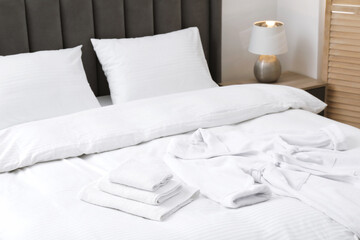 Comfortable bed with clean linens, pillows, towels and bathrobe indoors