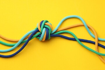 Colorful ropes tied in knot on yellow background, top view. Unity concept