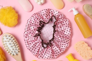 Shower cap and bath accessories on pink background, flat lay