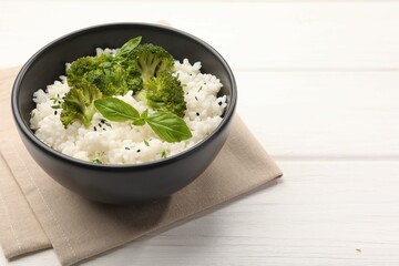 Tasty rice with broccoli and basil in bowl on white wooden table, closeup. Space for text
