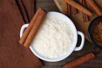 Delicious rice pudding with cinnamon sticks on wooden table, flat lay