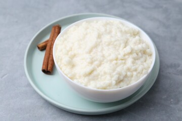 Delicious rice pudding with cinnamon sticks on grey table, closeup
