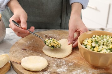 Woman making pirozhki (stuffed pastry pies) with eggs and dill at table indoors, closeup