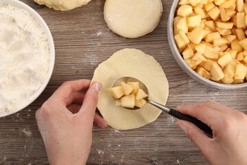 Woman making pirozhki (stuffed pastry pies) with apples at wooden table, top view