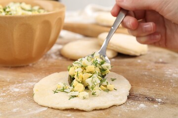 Woman making pirozhki (stuffed pastry pies) with eggs and dill at table, closeup