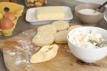 Making pirozhki (stuffed pastry pies). Pieces of dough with cottage cheese on wooden table, closeup