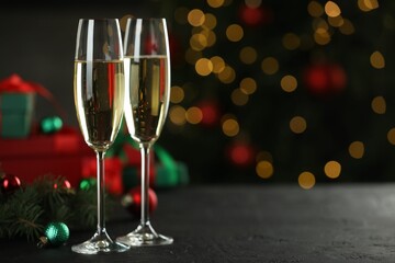 Champagne in glasses and decor on black table against blurred Christmas lights, space for text