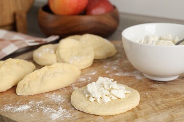 Making pirozhki (stuffed pastry pies). Pieces of dough with cottage cheese on wooden table, closeup