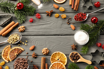 Frame of different aromatic spices and fir tree branches on grey wooden table, flat lay with space for text. Christmas season
