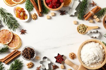 Frame of different aromatic spices and fir tree branches on white table, flat lay with space for text. Christmas season
