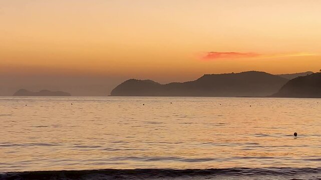 Final de tarde em tom laranja. O mar bem calmo e ao fundo, a "cabe&ccedil;a da baleia", montanha situada na praia da Baleia