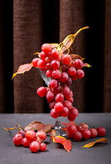 Bunch of vibrant red grapes displayed elegantly in glass, with autumn leaves scattered around on dark surface. Ideal for concepts of harvest, seasonal produce and healthy living