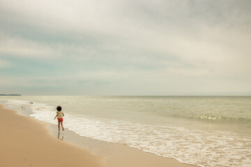 petite fille marchant seule au bord d'une plage vide
