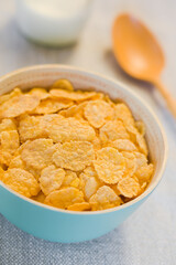 Crispy unsweetened corn flakes in blue bowl, milk and spoon in the back, photographed with natural light (Selective Focus, Focus one third into the bowl)